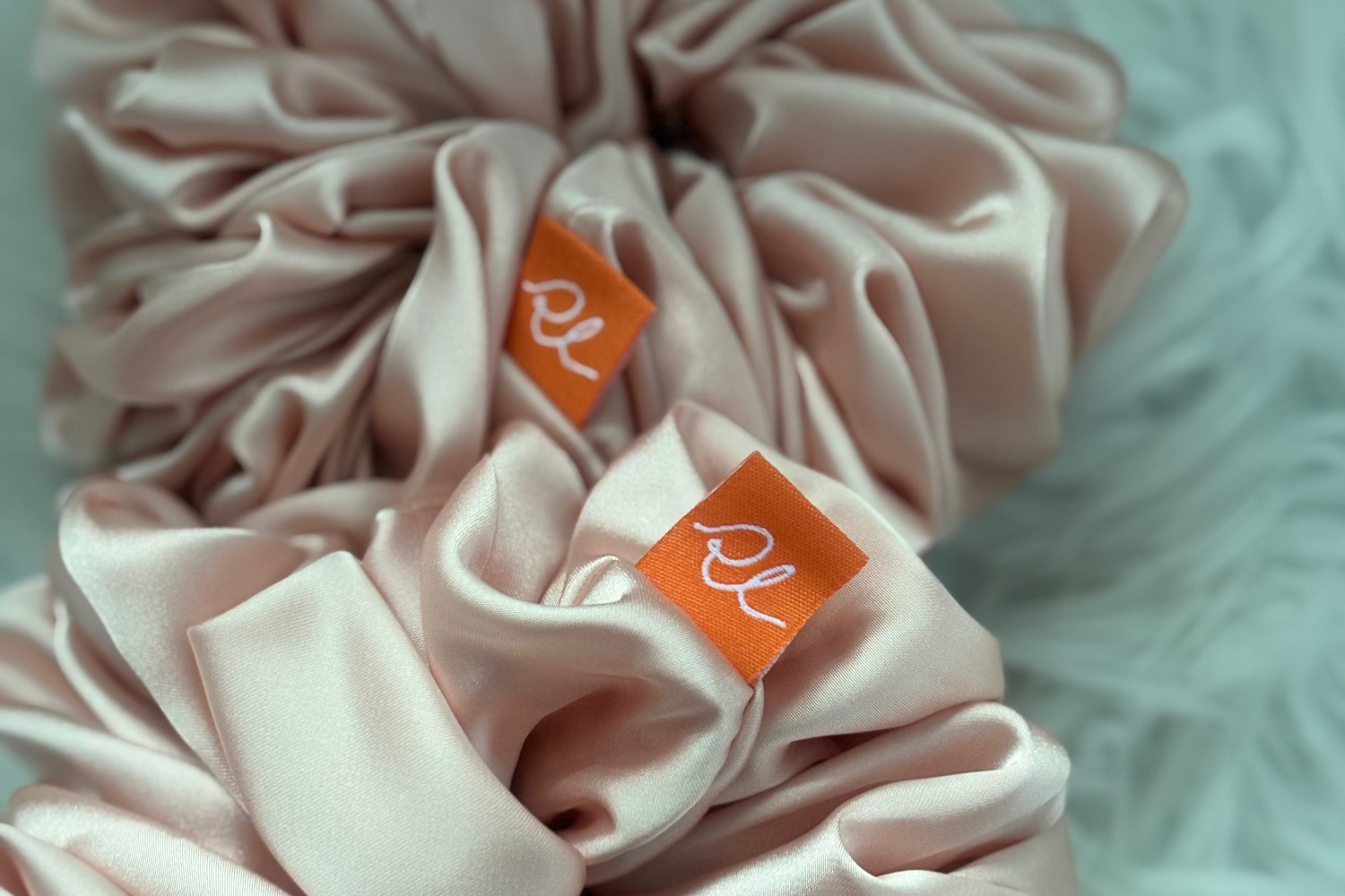 Two pink scrunchies with orange labels on a light background
